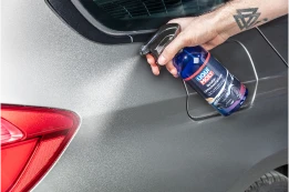 Eine Hand besprüht den grauen Lack eines Autos mit einer blauen Liqui Moly Sprühflasche zur Lackpflege.